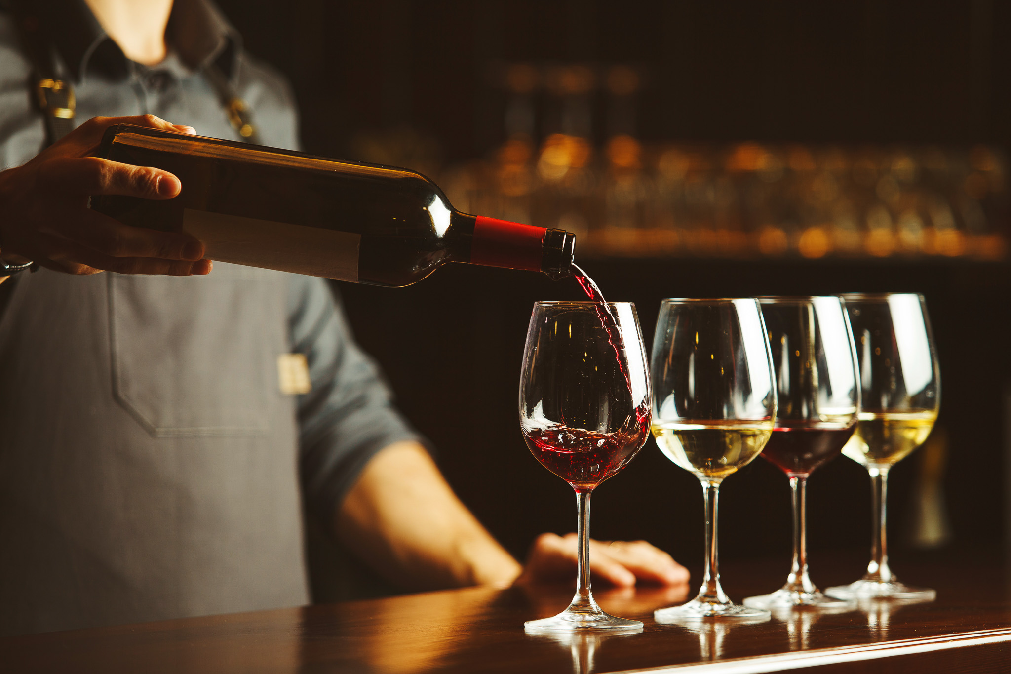 Bartender pours red wine in glasses on wooden bar counter